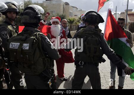 Bethlehem. 23. Dezember 2014. Palästinensische Demonstranten Weihnachtsmann Kostüme tragen Zusammenstoß mit israelischen Soldaten in einem israelischen Checkpoint in der West Bank von Bethlehem am 23. Dezember 2014. Der Protest soll Nachfrage freien Zugang nach Jerusalem in den Weihnachtsferien. © Luay Sababa/Xinhua/Alamy Live-Nachrichten Stockfoto