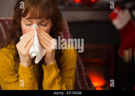 Frau sitzt auf dem Sofa und bläst ihre Nase zu Weihnachten Stockfoto