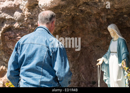 Mann, der betet vor der Statue der Jungfrau Maria Stockfoto