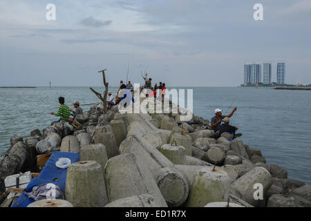 Menschen, die von Tetrapoden-Strukturen fischen, die den Fischereihafen Muara Angke als Wellenbrecher in Penjaringan, Jakarta, Indonesien, schützen. Stockfoto