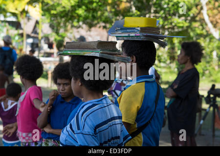 Melanesien, Papua Neu Guinea, Dobutamin Insel. Dorfschule. Schüler mit Schulbüchern auf ihren Köpfen. Stockfoto