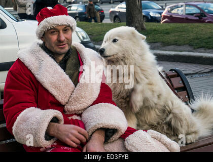 Kiew, Ukraine. 25. Dezember 2014. In Donnerstag, 25. Dezember 2014 sitzt auf Khreschatyk Street, Kiew, Ukraine, einen jungen Mann mit weißen flauschigen Hunde als Weihnachtsmann verkleidet. Bildnachweis: Igor Golovnov/Alamy Live-Nachrichten Stockfoto