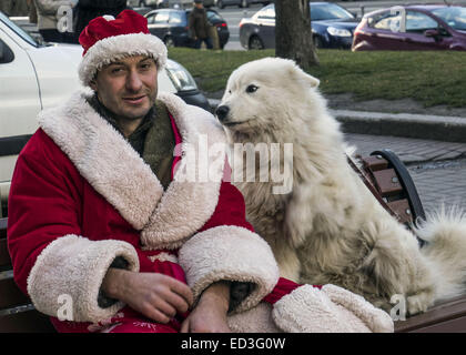 In Donnerstag, 25. Dezember 2014 sitzt auf Khreschatyk Street, Kiew, Ukraine, einen jungen Mann mit weißen flauschigen Hunde als Weihnachtsmann verkleidet. 25. Dezember 2014. © Igor Golovniov/ZUMA Draht/Alamy Live-Nachrichten Stockfoto