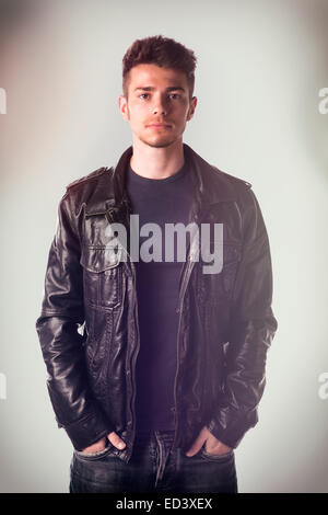 Attraktiver junger Mann mit Lederjacke und Hände in den Jeanstaschen, Blick in die Kamera Stockfoto