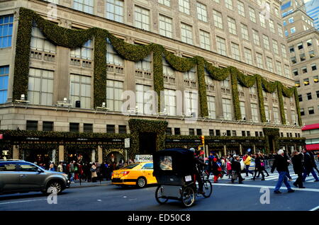 New York City: Ein Rikscha Taxi übergibt legendäre Saks Fifth Avenue-Kaufhaus, geschmückt mit Weihnachtsschmuck Stockfoto