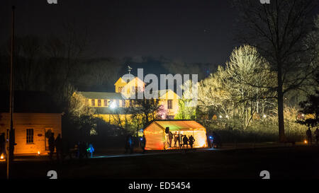 Alten Bethpage, New York, USA. 26. Dezember 2014. Am Abend sind die historischen, geschwungene rustikalen Gelände des alten Bethpage Village Restaurierung bei Kerzenschein und Weihnachtsschmuck in ein 19. Jahrhundert Urlaubserlebnis für Long Island Besucher verwandelt. Familienspaß inklusive Nachbildungen von 1800 Musik mit einem Trio von Sängern in einem offenen vorderen Zelt, gesehen in diesem Panorama. Candle-Light-Abende sind bis zum 30. Dezember statt. Stockfoto