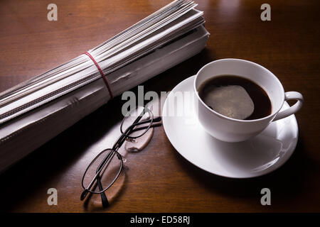 Zeitung, Gläser und Becher Kaffee am Schreibtisch Stockfoto