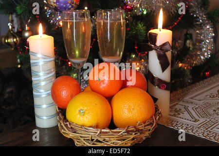 zwei Kristallglas voller Süße goldenen Sekt, Obst im Korb und drei brennende Kerzen Stockfoto