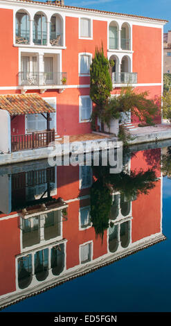 Eine kleine rote typische Gebäude von Port Grimaud, in Südfrankreich, spiegelt sich in dem ruhigen Wasser eines Kanals Stockfoto