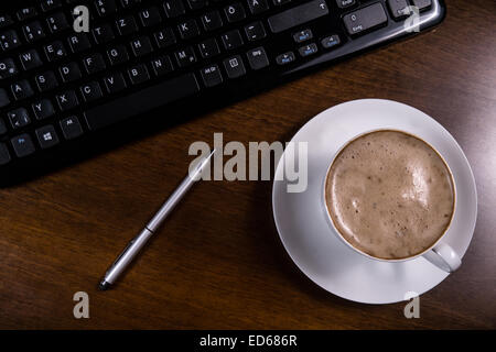 Tasse Kaffee, Tastatur und Stift auf Schreibtisch Stockfoto