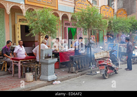 Uyghur Männer essen Fleisch vom Grill im Freien in kleinen traditionellen Restaurant in der Stadt Kashgar / Kashi, Provinz Xinjiang, China Stockfoto