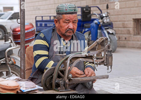 Schuhmacher / Schuh Handwerker bei der Arbeit auf der Straße in Qiemo / Cherchen, Oasenstadt in der Taklamakan-Wüste, Provinz Xinjiang, China Stockfoto