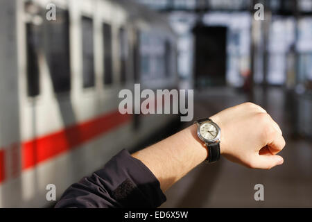 Metapher-Bild für einen Zug Verspätung: Mann prüft seine Uhr auf dem Bahnsteig; Im Hintergrund steht ein Zug warten Stockfoto