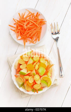 Obstsalat mit Karotten, Äpfel, Bananen und Cornflakes in Schüssel auf weißer Holztisch, Ansicht von oben Stockfoto