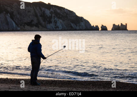 Ein Mann mit einem "Selfie Stick" in Alum Bay auf der Isle Of Wight mit den Nadeln in der Ferne Stockfoto