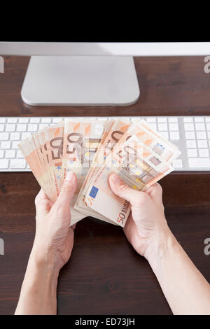 Frau übergibt Tastatur Computer braun Holztisch zählen fünfzig Euro-Banknoten Stockfoto