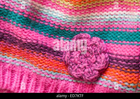 Nahaufnahme Detail Bunte gestrickte gestreifte Babymütze mit gehäkelten Blume Stockfoto