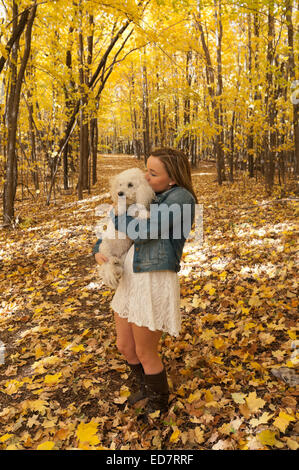 in voller Länge Portrait von junge weibliche Teenager auf Waldweg küssen Hund im Herbst Stockfoto