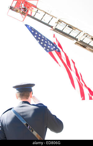 Ein Polizist begrüßte die amerikanische Flagge, die von einer Feuerwehr Leiter aufgehängt Stockfoto