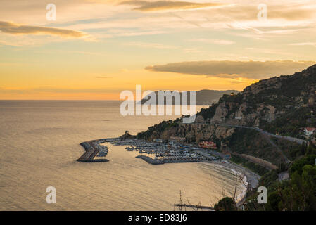 Die dramatische Felsenküste in Ligurien, Italien, mit einer kleinen Bucht und Pier im Vordergrund. Bunte Horizont auf dem Meer auf Dämme Stockfoto