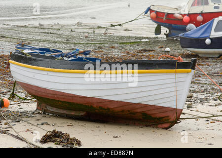 Kleine weiße Fischerboot am Strand bei Ebbe im Hafen von Mousehole, Cornwall, England Stockfoto
