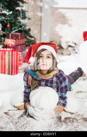 Schöne junge Frau in eine Weihnachtsmütze auf dem Boden in der Nähe von Christmas tree Stockfoto