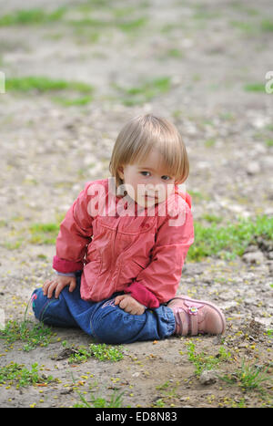 Kleines Mädchen sitzt auf dem Boden etwas befasst sich mit der Seite. Stockfoto