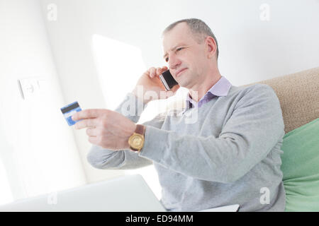 Erwachsener Mann liest eine Kreditkarten-Nummer beim Anruf Stockfoto