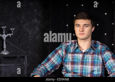 Der junge Mann sitzt in Plüsch schwarz hohe Rückenlehne Stuhl im Spukhaus Einstellung hautnah Stockfoto