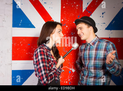 Junge Frau interviewt glücklich junge Mann trendige Mode mittels Mikrofon, vor britischen Flagge drucken hautnah. Stockfoto