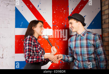 Froh, dass Interviewer Frau mit Mikrofon schütteln Hände mit Gast in modischen vor britischen Flagge drucken. Stockfoto
