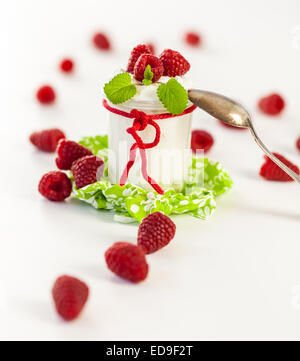 Frische reife Himbeeren serviert mit einem Glas des gesunden Joghurt oder Clotted Cream für ein leckeres Dessert oder Frühstück mit Exemplar Stockfoto