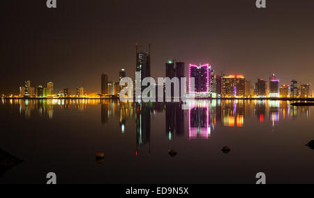 Nacht Skyline der modernen Stadt mit leuchtenden Neonröhren und Spiegelungen im Wasser. Manama, Bahrain, Naher Osten Stockfoto
