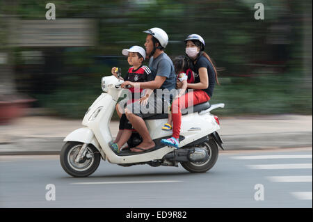 Vier-Personen-Familie auf dem Roller Motorrad in Ho-Chi-Minh-Stadt Vietnam zwei junge Kinder essen nicht tragen Helme Stockfoto