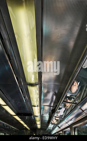 Passagiere und ein Geschäftsmann, der während der Fahrt mit dem Zug an einem Laptop arbeitet, spiegeln sich im polierten Dach des Wagens wider (UK) Stockfoto