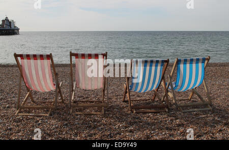 Vier leer Liegestühle am Strand von Brighton Seeseite mit Helter Skelter am Pier in Ferne Stockfoto