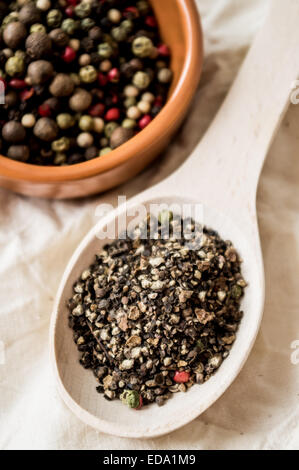 Mischung aus gemahlenen Pfeffer in einem Holzlöffel und ganze Paprika in eine Schüssel geben Stockfoto
