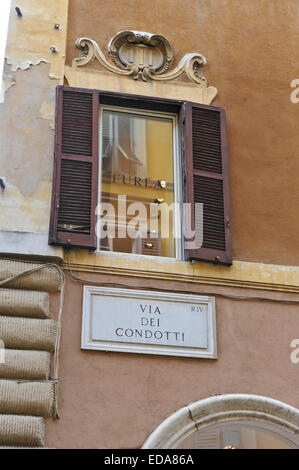 Ein offenes Fenster mit hölzernen Auslöser über die berühmte Via dei Condotti Straßenschild, Rom, Italien. Stockfoto