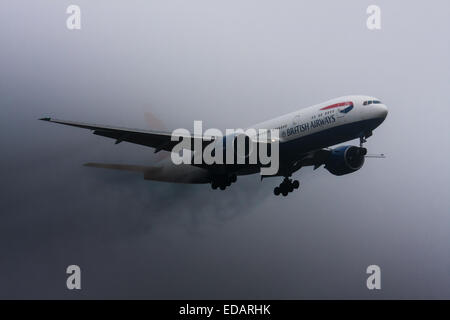 3. Januar 2015, Heathrow Airport, London. Niedrige Wolken und Regen bieten ideale Voraussetzungen Gefolge Wirbel und "Flusen" kondensiert Feuchtigkeit über die Flügel von landenden Flugzeuge zu beobachten. Mit der Start-und Landebahn sichtbar nur in letzter Minute mussten mehrere Flugzeuge ein "Go-Round", Verzicht auf ihre ersten Versuche landen zu leisten. Bild: Eine British Airways Boeing 777 ergibt sich aus der niedrigen Wolken, Streaming-Wasserdampf, kurz vor der Landung am Flughafen Heathrow Start-und Landebahn 27L Stockfoto