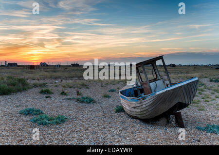 Einem alten hölzernen Fischerboot auf Schindel in Kent unter einem dramatischen Sonnenuntergang Himmel gestrandet Stockfoto