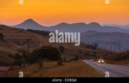 Swasiland, Afrika - Holz-Feuer Rauch erzeugt orange Sonnenuntergang über Berglandschaft, als die Autos fahren auf der Autobahn. Stockfoto