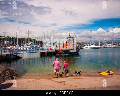 Zwei Männer zu Fuß ihre Hunde, bewundern Sie die Rnli lifeboat außerhalb Torbay Rettungsboot Station, Brixham, Großbritannien. Stockfoto
