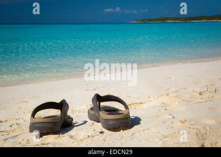 Flip Flops an einem Sandstrand mit türkisfarbenem Wasser hinaus Halfmoon Cay, Bahamas Stockfoto