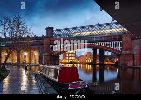 Castlefield Bassin Bereich von Manchester in der Abenddämmerung, ein Kanal Narrowboat Partie am Bridgewater Kanal mit Eisenbahnviadukt hinter Stockfoto