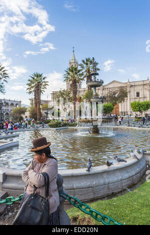 Alte Frau in traditioneller Kleidung und Hut an einem Brunnen in Plaza de Armas, Arequipa, Peru Stockfoto