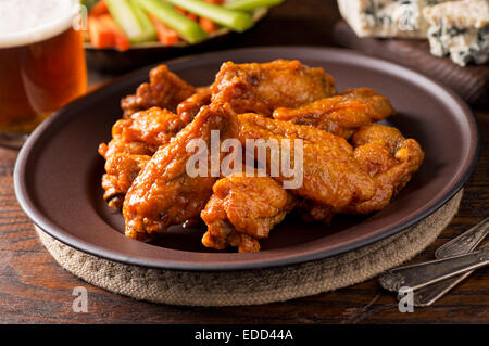 Eine Platte von köstlichen Buffalo Style Chicken Wings mit scharfer Sauce, Blauschimmelkäse, Stangensellerie, Karotten-Sticks und Bier. Stockfoto
