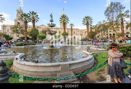 Frau in traditioneller Kleidung und Hut an einem Brunnen in Plaza de Armas, Arequipa, Peru Stockfoto