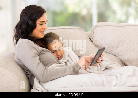 Mutter mit Tochter schlafen auf der Couch sitzen und Tablettcomputer verwenden Stockfoto