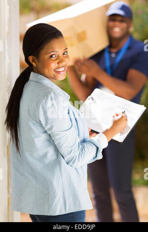 hübsche schwarze Frau unterschreiben für den Empfang von Paket Stockfoto