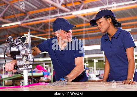 freundlichen senior Cutter Unterrichten junger Arbeiter Schneiden Stoff Stockfoto